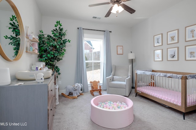 bedroom featuring light carpet, visible vents, a crib, and a ceiling fan