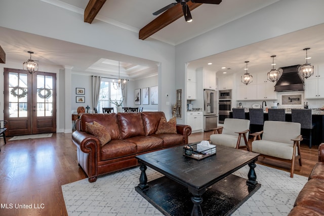 living area featuring beam ceiling, wood finished floors, crown molding, and ceiling fan with notable chandelier