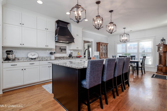 kitchen with a kitchen bar, a notable chandelier, custom range hood, stainless steel gas stovetop, and light wood finished floors