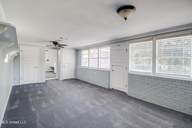 unfurnished living room with ceiling fan, crown molding, brick wall, and dark colored carpet