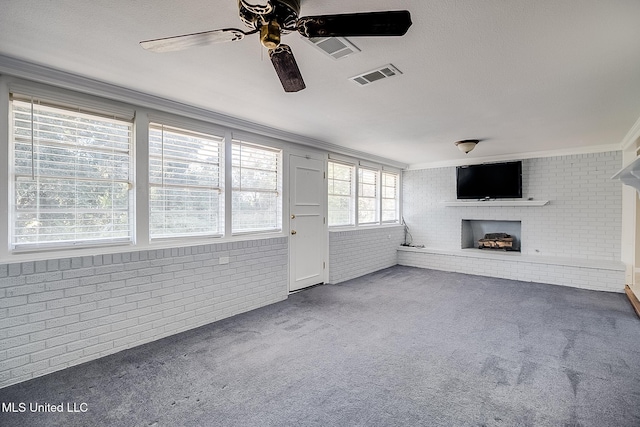 unfurnished living room with a brick fireplace, ornamental molding, brick wall, ceiling fan, and carpet floors