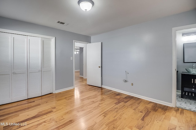 unfurnished bedroom with ensuite bathroom, a closet, sink, and light hardwood / wood-style flooring