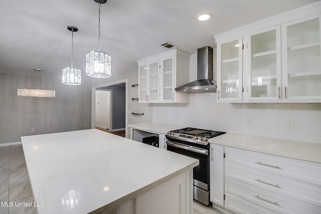 kitchen featuring wall chimney exhaust hood, stainless steel gas range oven, a kitchen island, and white cabinetry