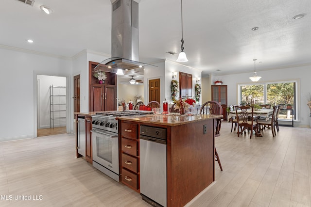 kitchen with hanging light fixtures, island range hood, a center island with sink, high end range, and ornamental molding