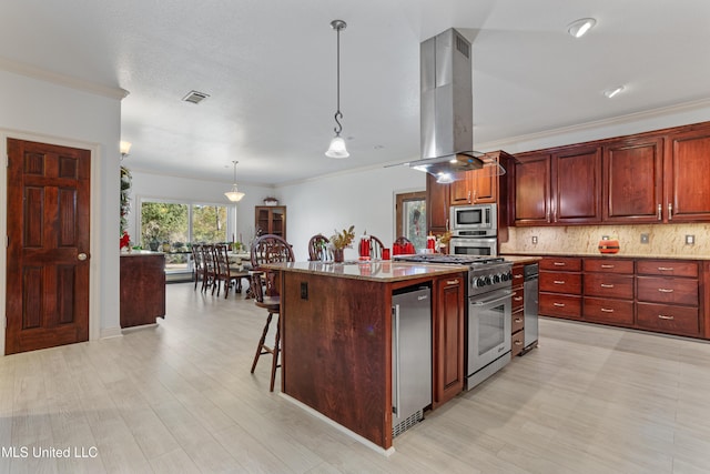 kitchen featuring appliances with stainless steel finishes, a kitchen breakfast bar, island range hood, pendant lighting, and an island with sink