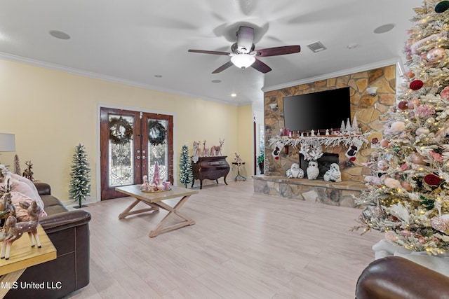 living room featuring ceiling fan, light hardwood / wood-style floors, a stone fireplace, and crown molding