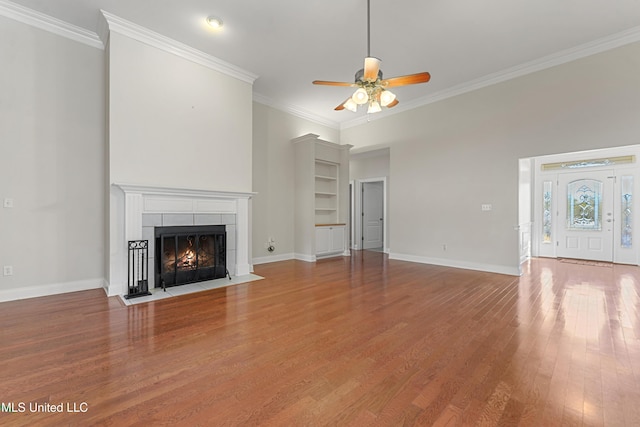 unfurnished living room with ceiling fan, hardwood / wood-style floors, ornamental molding, and a tiled fireplace