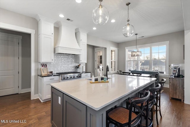 kitchen with custom range hood, a center island with sink, a kitchen bar, and white cabinetry