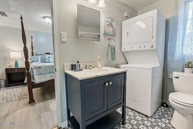 bathroom with hardwood / wood-style floors, a textured ceiling, toilet, vanity, and stacked washer / dryer