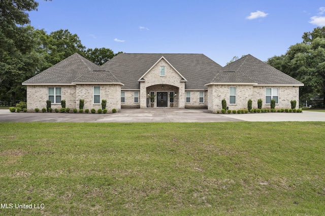 french country home with roof with shingles, a front lawn, and brick siding