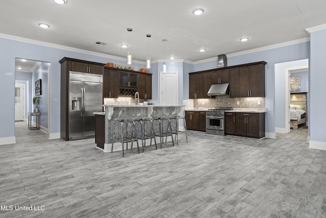kitchen with high end appliances, under cabinet range hood, a kitchen bar, dark brown cabinets, and tasteful backsplash