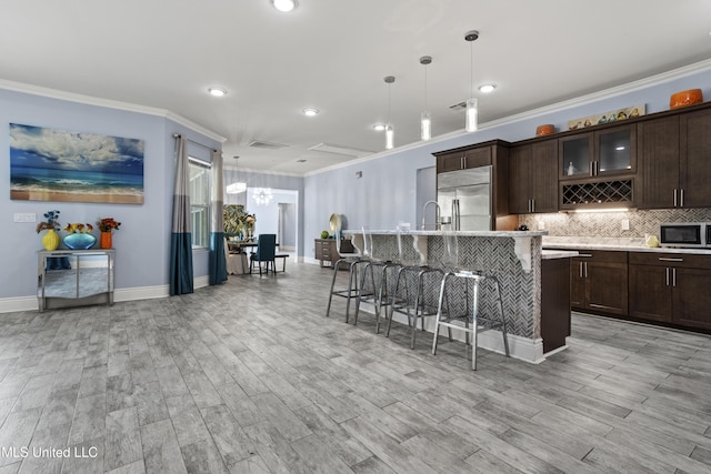 kitchen featuring appliances with stainless steel finishes, ornamental molding, light countertops, a kitchen breakfast bar, and dark brown cabinets