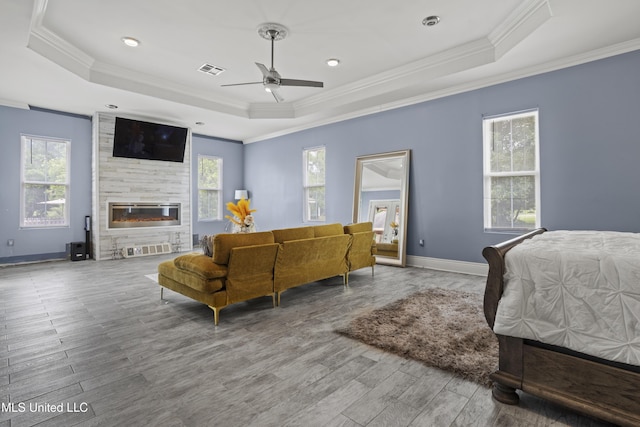 bedroom featuring a raised ceiling, crown molding, wood finished floors, a fireplace, and baseboards