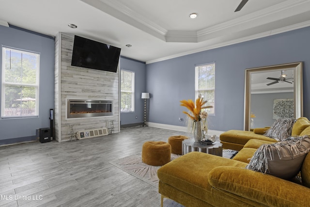 living room featuring a ceiling fan, crown molding, a fireplace, wood finished floors, and baseboards