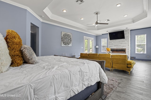 bedroom featuring multiple windows, a tray ceiling, ornamental molding, wood finished floors, and a fireplace