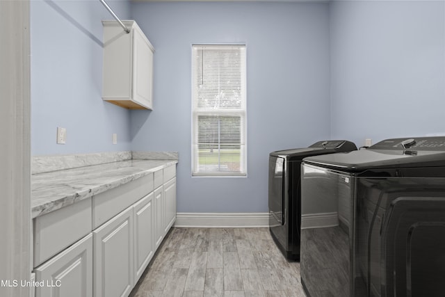 laundry area featuring independent washer and dryer, cabinet space, light wood-style floors, and baseboards