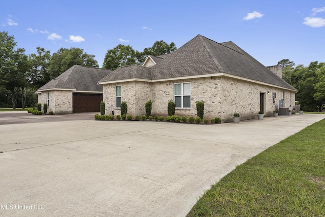 view of front of property with central air condition unit, brick siding, a garage, a shingled roof, and concrete driveway