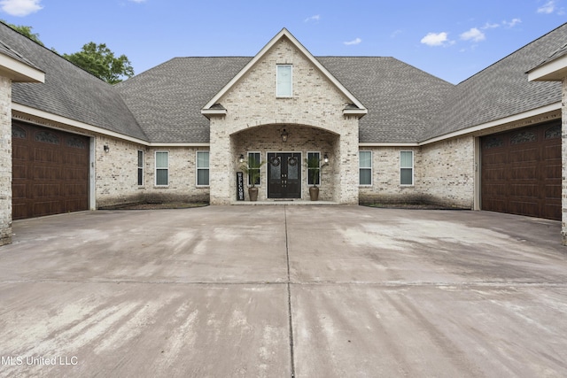 property entrance featuring french doors, brick siding, and roof with shingles
