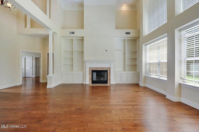 unfurnished living room featuring built in features, a towering ceiling, and hardwood / wood-style floors