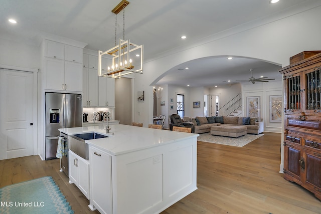 kitchen with pendant lighting, sink, stainless steel fridge, white cabinetry, and a kitchen island with sink