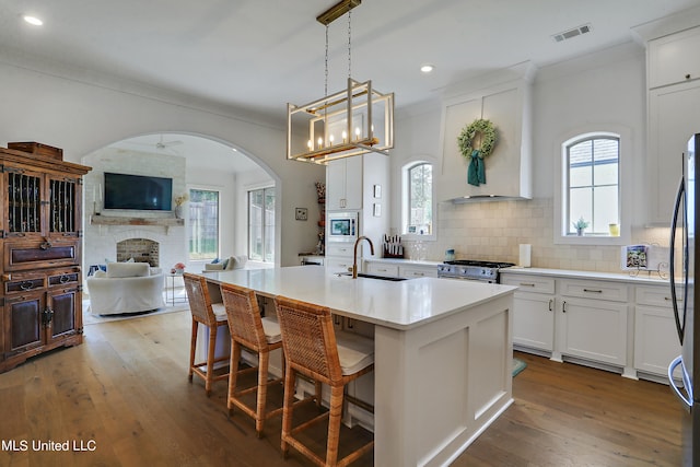 kitchen with sink, hanging light fixtures, white cabinets, a center island with sink, and a brick fireplace