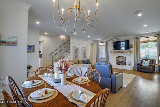 dining room with ornamental molding, a brick fireplace, ceiling fan with notable chandelier, and light hardwood / wood-style floors