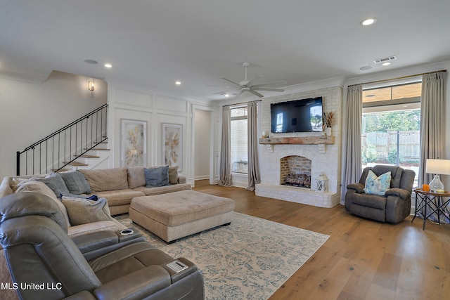 living room featuring a fireplace, wood-type flooring, ornamental molding, and ceiling fan