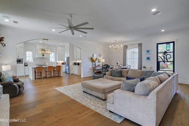 living room with sink, ceiling fan with notable chandelier, and light wood-type flooring