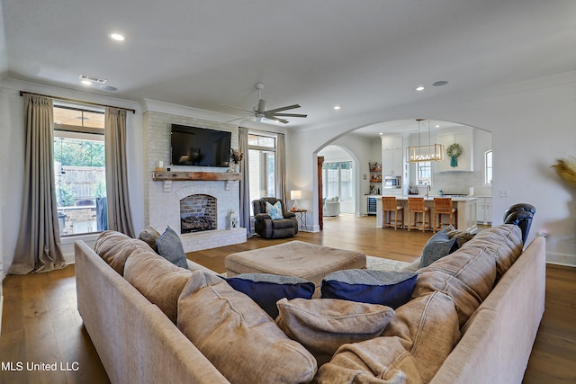 living room with ornamental molding, a brick fireplace, and light wood-type flooring