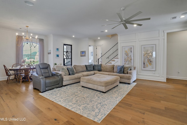 living room with ceiling fan with notable chandelier, ornamental molding, and hardwood / wood-style floors