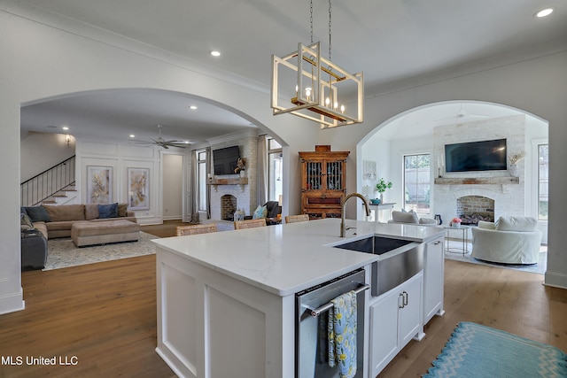 kitchen featuring a fireplace, white cabinetry, an island with sink, sink, and hanging light fixtures