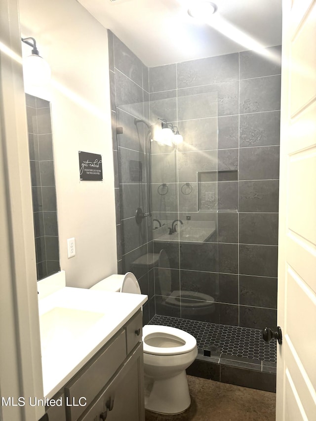 bathroom featuring vanity, a tile shower, and toilet