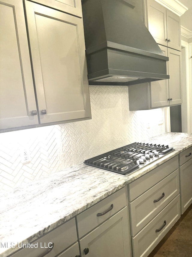 kitchen featuring tasteful backsplash, premium range hood, stainless steel gas stovetop, light stone countertops, and gray cabinets