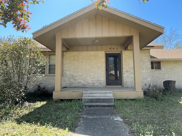 view of exterior entry with brick siding and covered porch