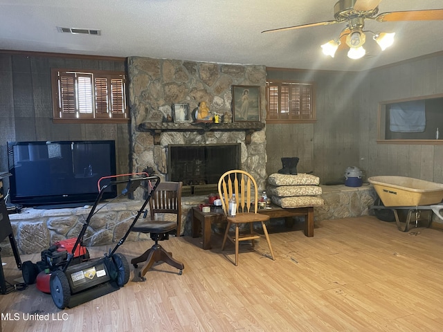 living room featuring wood finished floors, visible vents, a fireplace, ceiling fan, and a textured ceiling