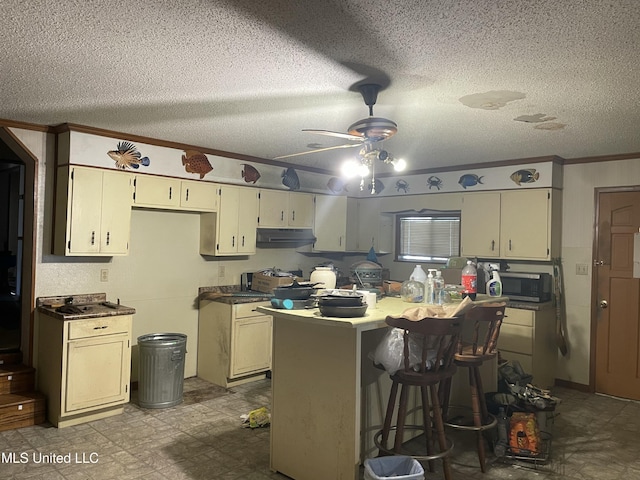 kitchen with ornamental molding, under cabinet range hood, stainless steel microwave, a kitchen breakfast bar, and a textured ceiling