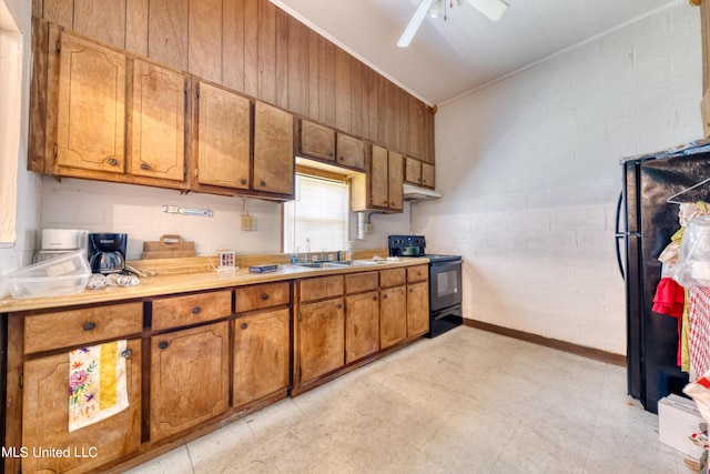 kitchen with a sink, brown cabinetry, ornamental molding, black appliances, and under cabinet range hood