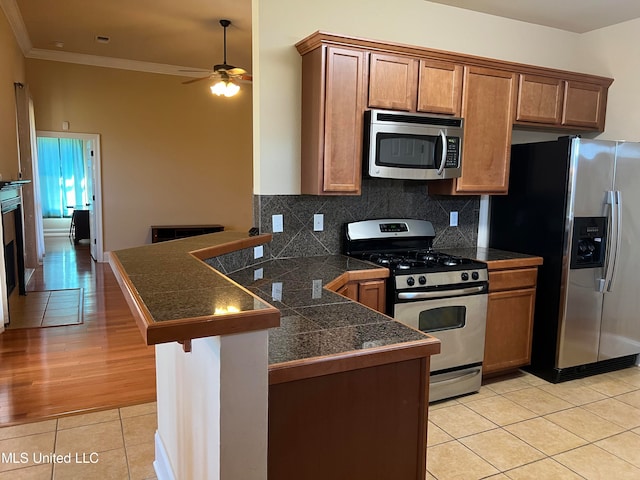 kitchen featuring light wood-type flooring, kitchen peninsula, ceiling fan, stainless steel appliances, and crown molding