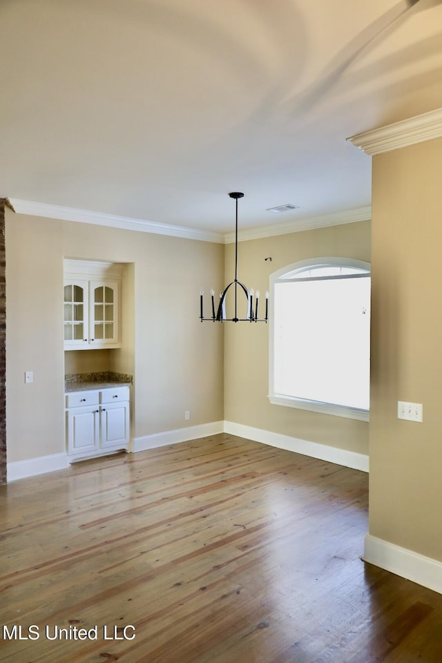 unfurnished dining area with baseboards, a notable chandelier, and crown molding