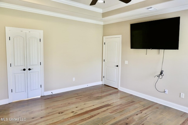 unfurnished bedroom featuring light wood-style flooring, a tray ceiling, crown molding, visible vents, and baseboards