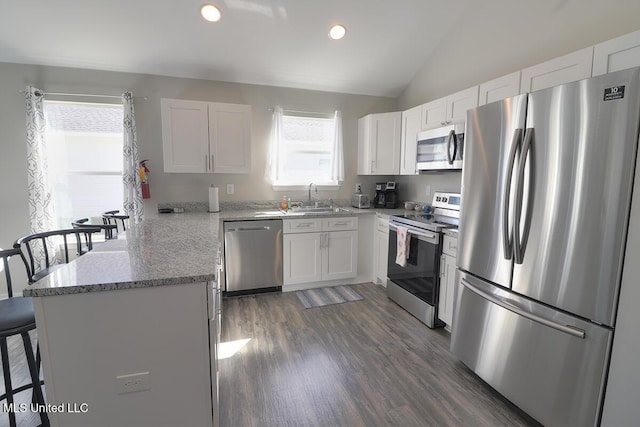 kitchen featuring a breakfast bar, appliances with stainless steel finishes, white cabinetry, vaulted ceiling, and a sink