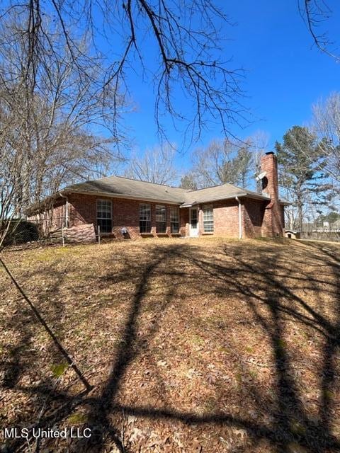 back of house with a chimney and brick siding