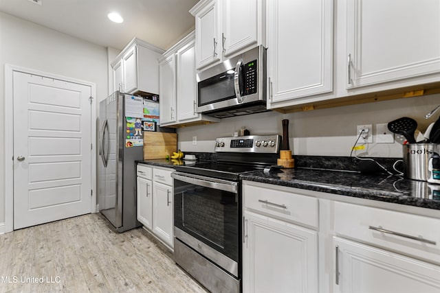 kitchen with stainless steel appliances, dark stone countertops, white cabinets, and light wood-type flooring