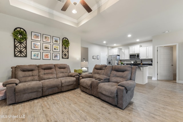 living room featuring ornamental molding, light hardwood / wood-style floors, ceiling fan, and a raised ceiling