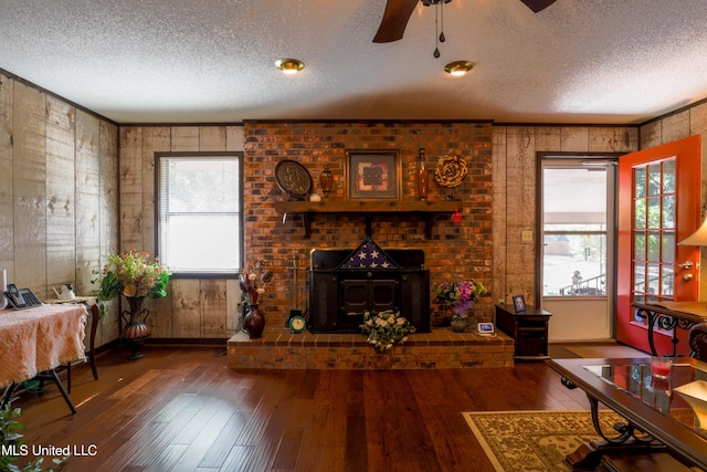 living room with dark wood-type flooring, ceiling fan, a textured ceiling, and a wood stove