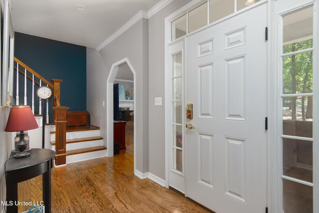 entrance foyer featuring wood finished floors, arched walkways, crown molding, baseboards, and stairs