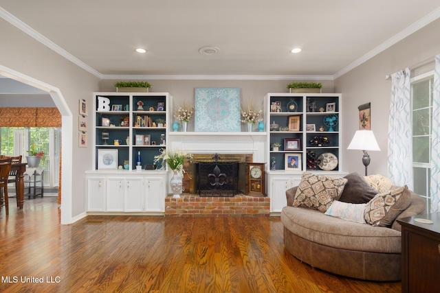 living room featuring a brick fireplace, wood finished floors, arched walkways, and crown molding