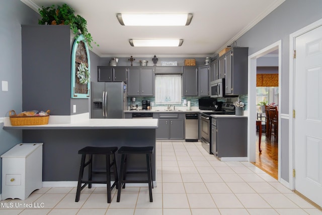 kitchen with a peninsula, a kitchen bar, crown molding, light countertops, and appliances with stainless steel finishes