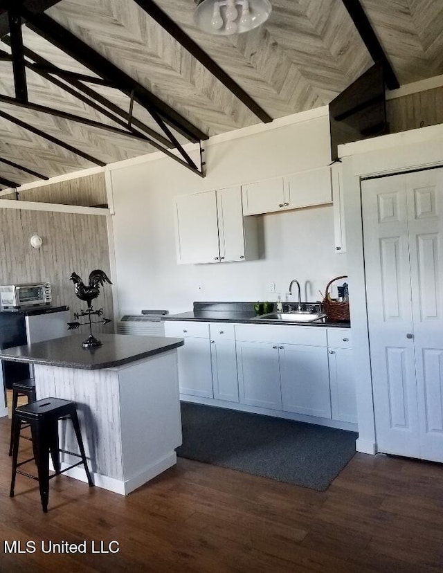 kitchen featuring dark wood-style floors, dark countertops, white cabinets, a sink, and wooden walls