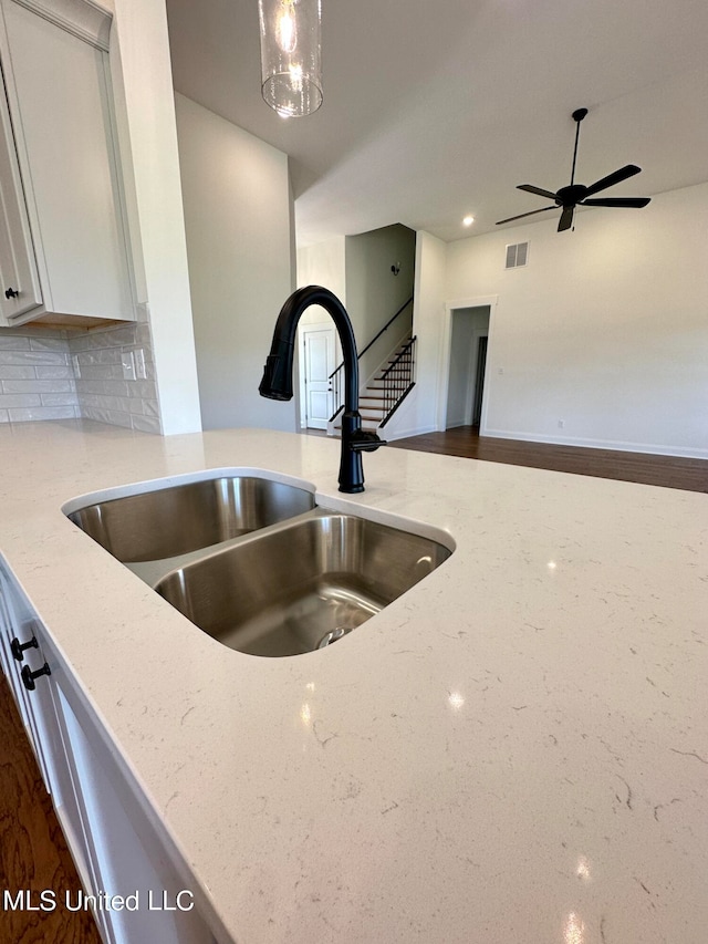 interior details with sink, backsplash, hanging light fixtures, white cabinets, and light stone counters